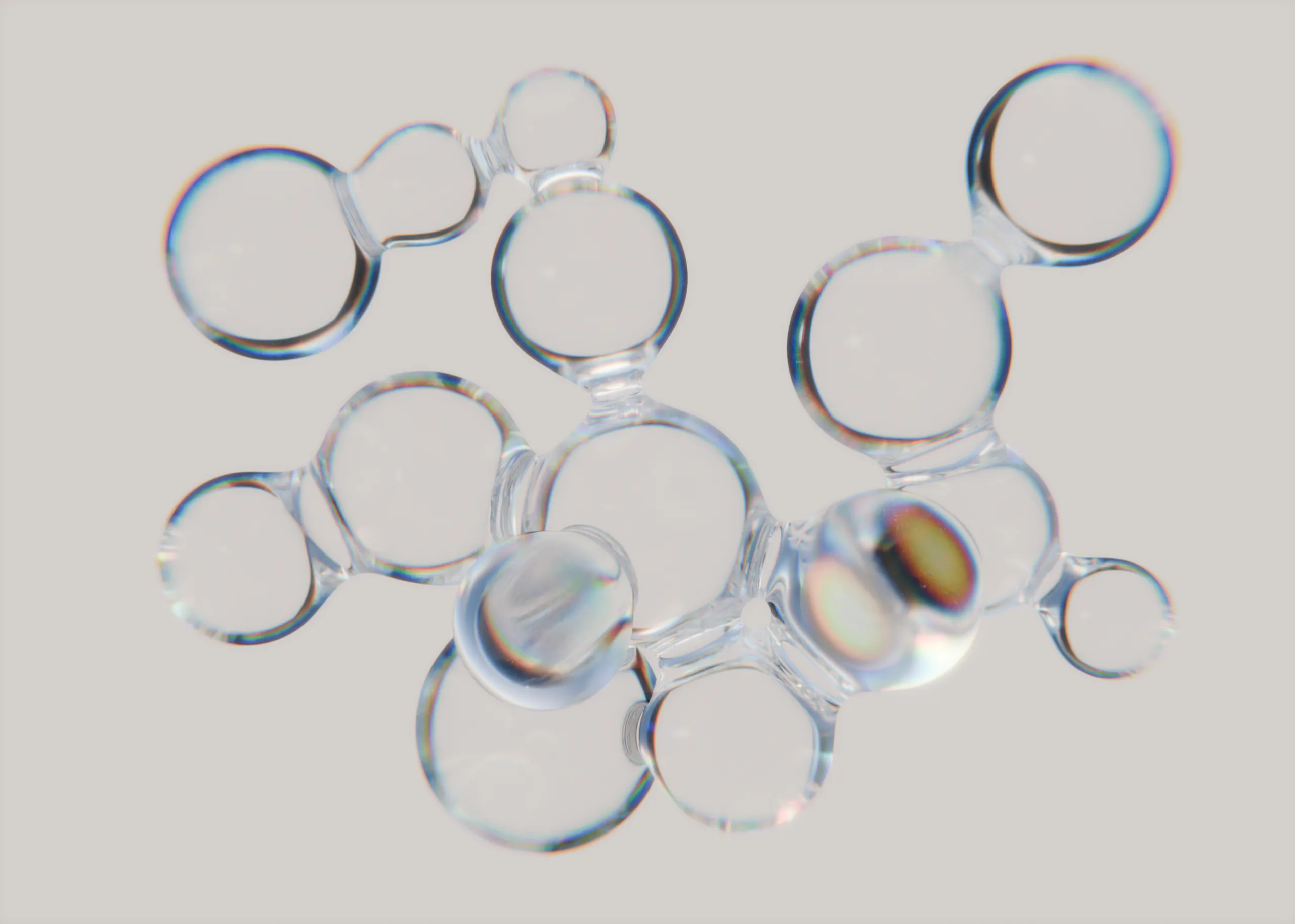 A cluster of clear connected bubbles showing rainbow dispersion on a pale ground