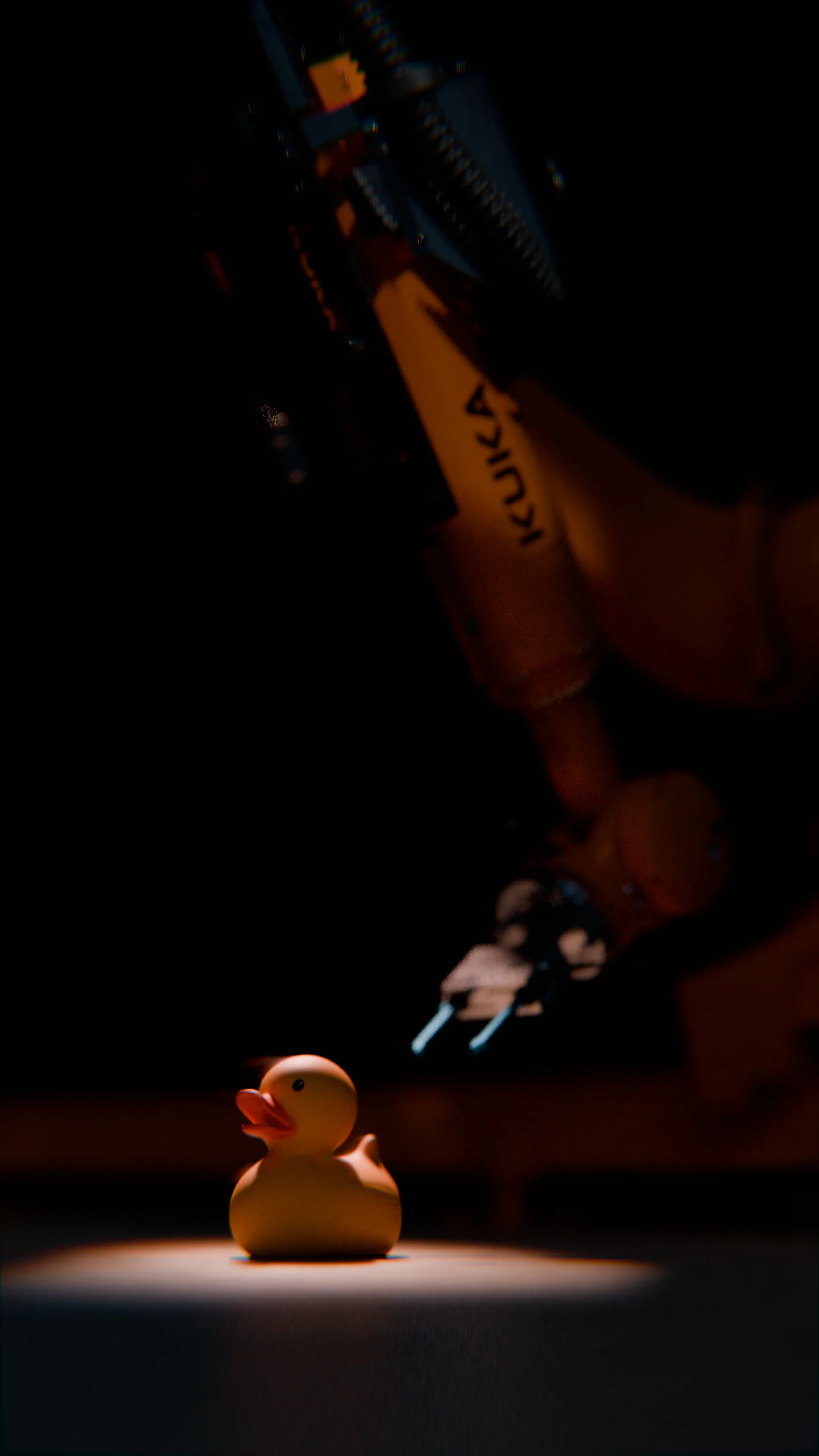 A rubber duck in a spotlight beneath a KUKA industrial robot arm